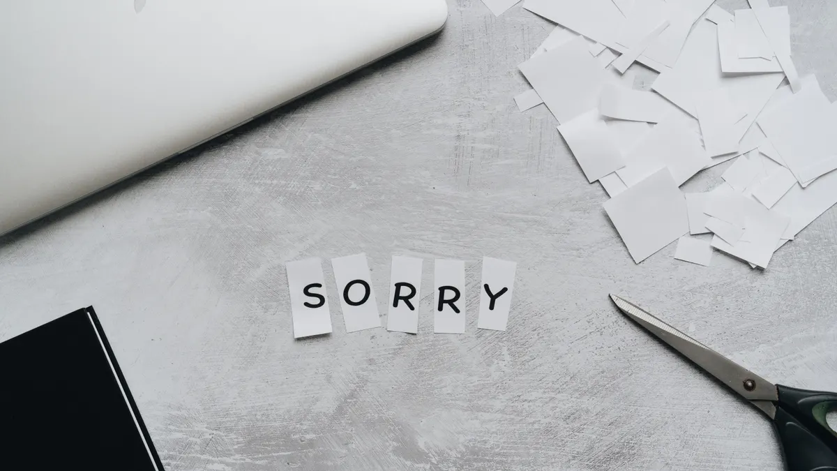 Vue de dessus d’un bureau avec lettres découpées « sorry », ciseaux et ordinateur portable ; mot en papier blanc.