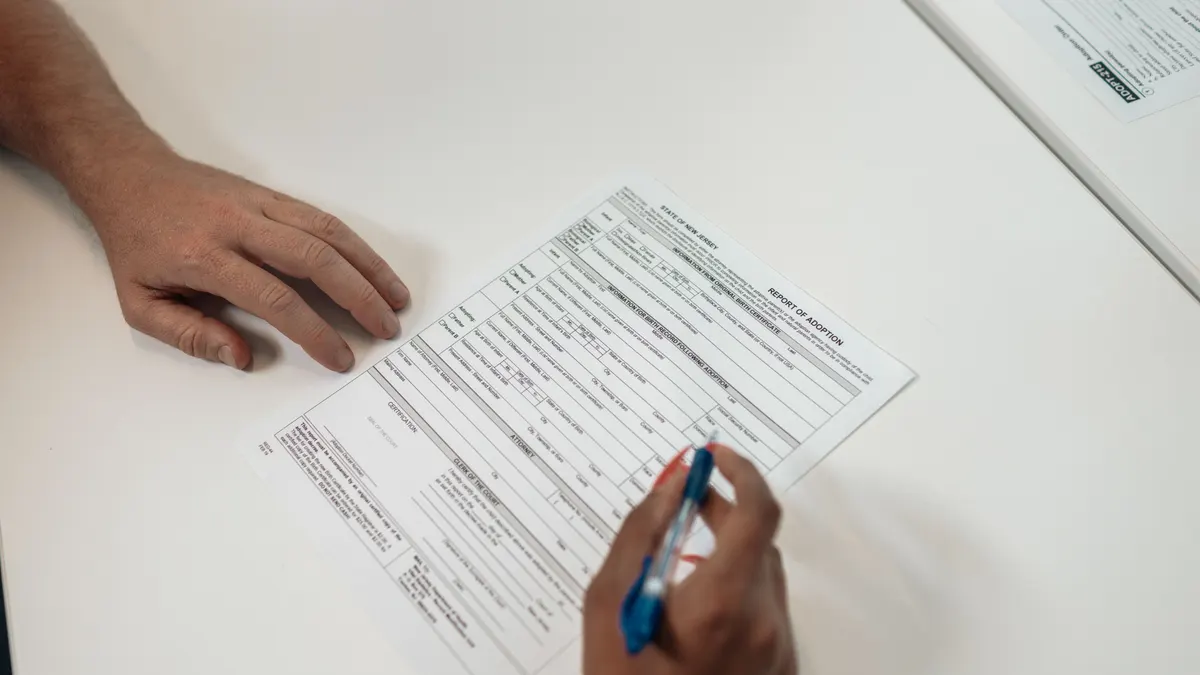 Deux personnes examinent et signent des documents d'adoption, une personne écrit sur du papier blanc.