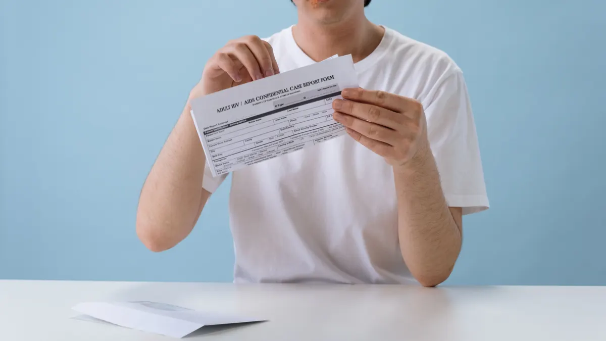 Homme en t-shirt blanc tenant un formulaire papier confidentiel sur le VIH/sida, fond bleu, à l'intérieur.