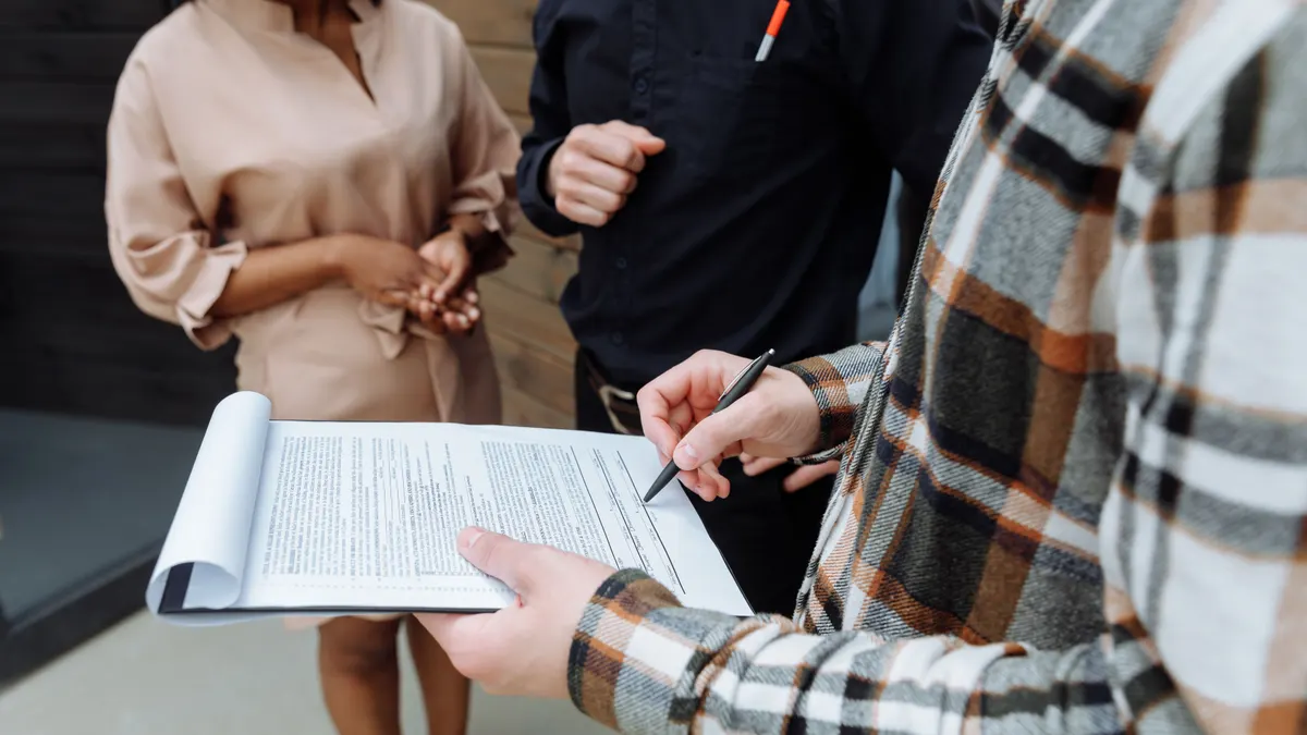 Trois adultes dans un bureau discutent et signent un document ; une personne signe un document.