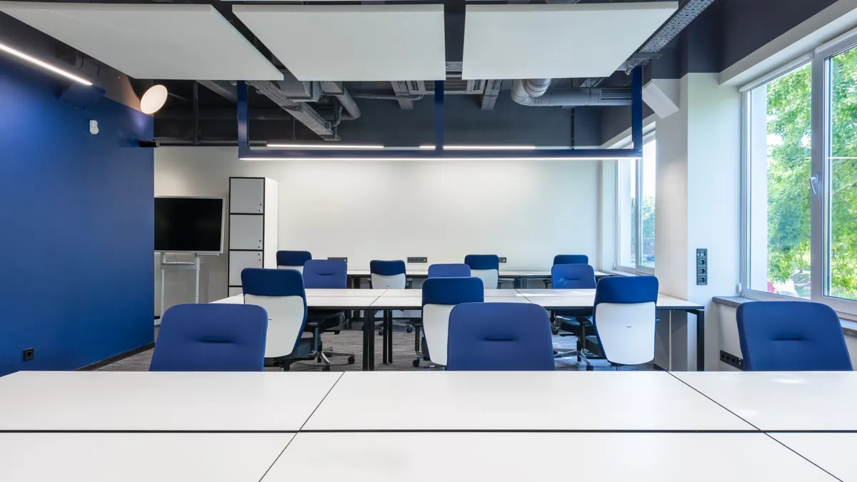 Bureaux blancs et chaises bleues dans un open space moderne spacieux avec grande fenêtre, écran et tables.