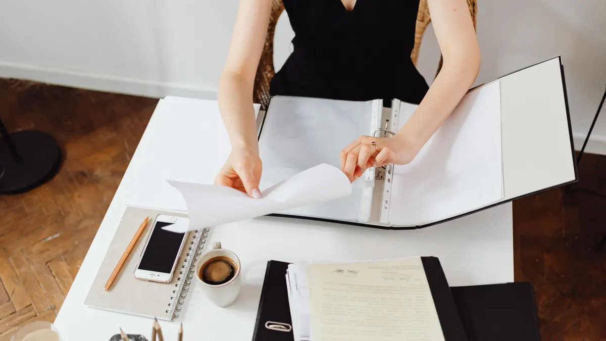 Professionnel travaillant avec des documents à un bureau, café et smartphone, pliant une feuille de papier blanche.