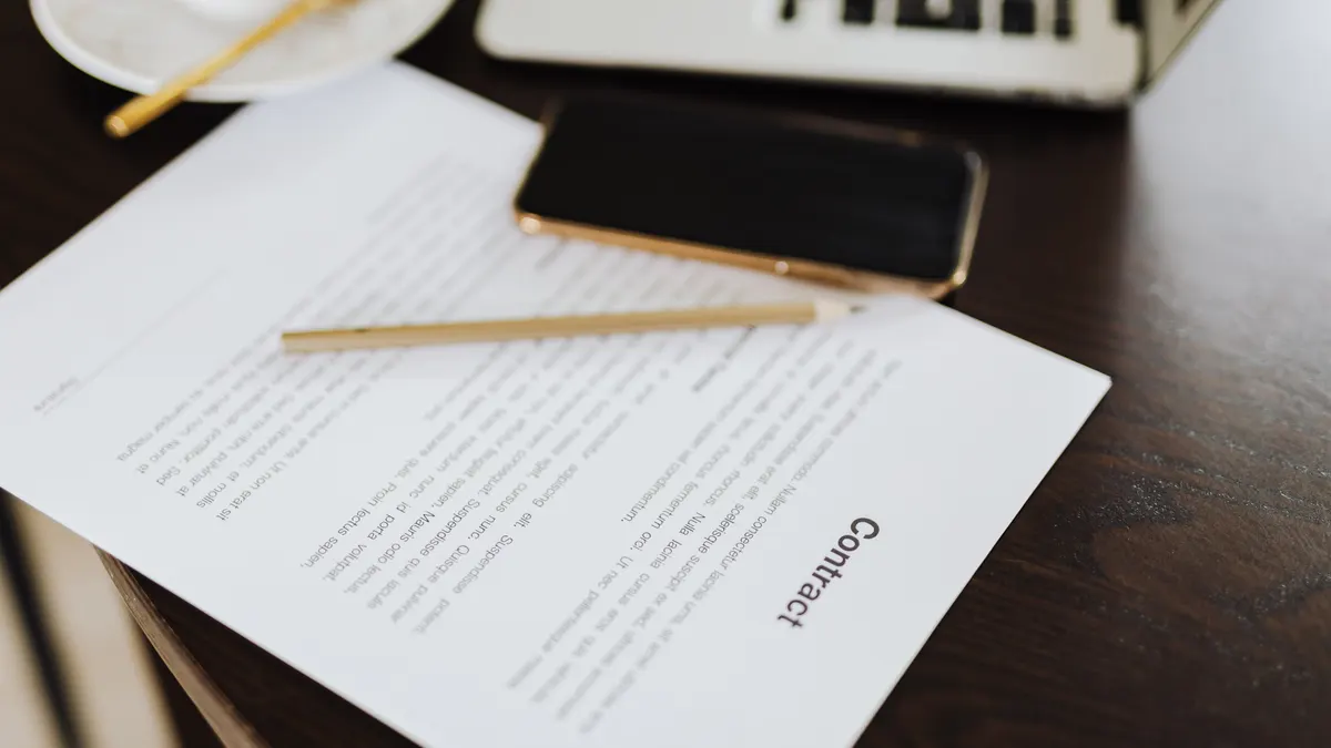 Gros plan d'un contrat avec ordinateur portable et café sur un bureau, et contrat avec téléphone mobile sur une table.