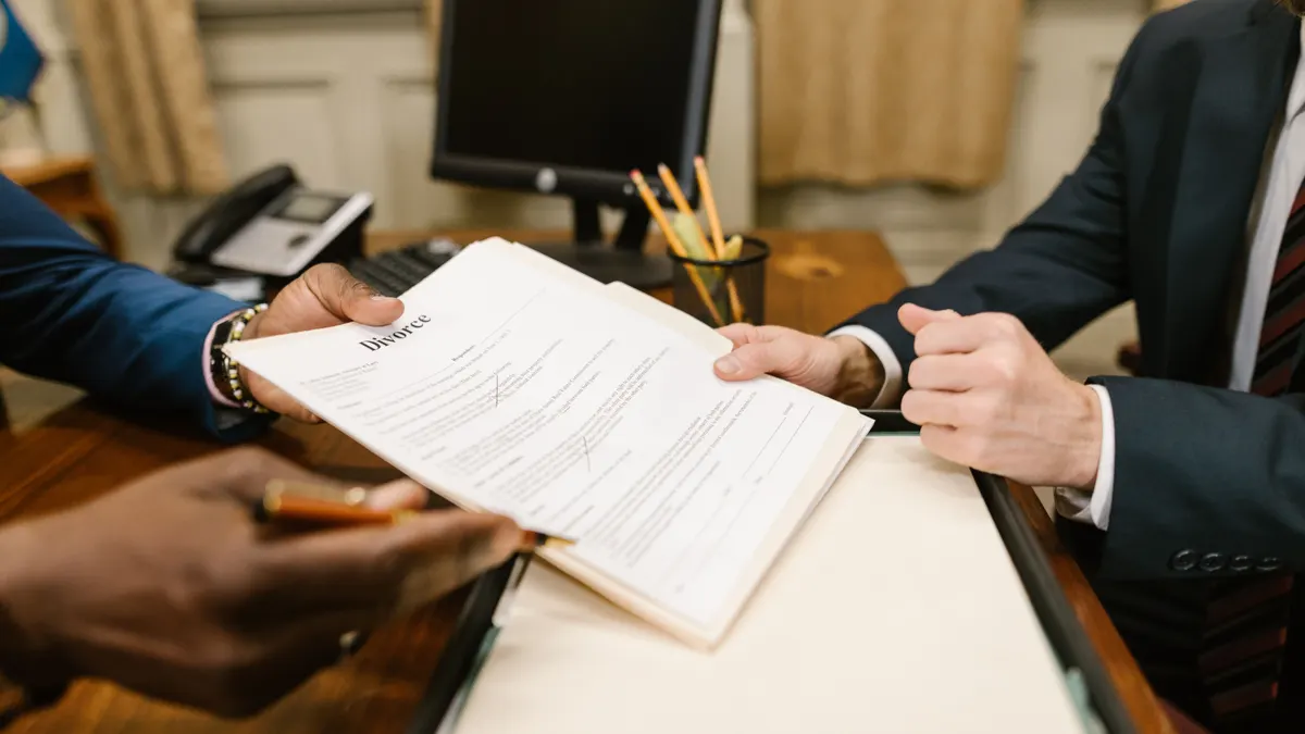 Gros plan de mains échangeant des documents de divorce dans un bureau.